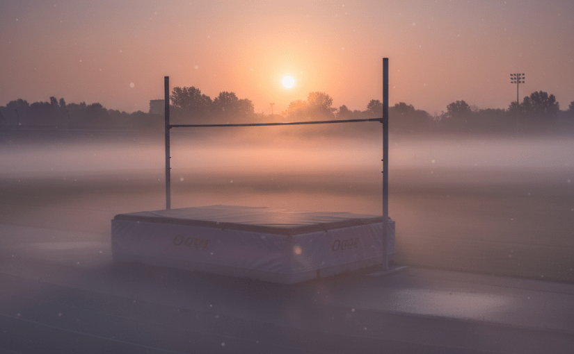 High jump mat and bar on track field covered in morning fog at sunrise
